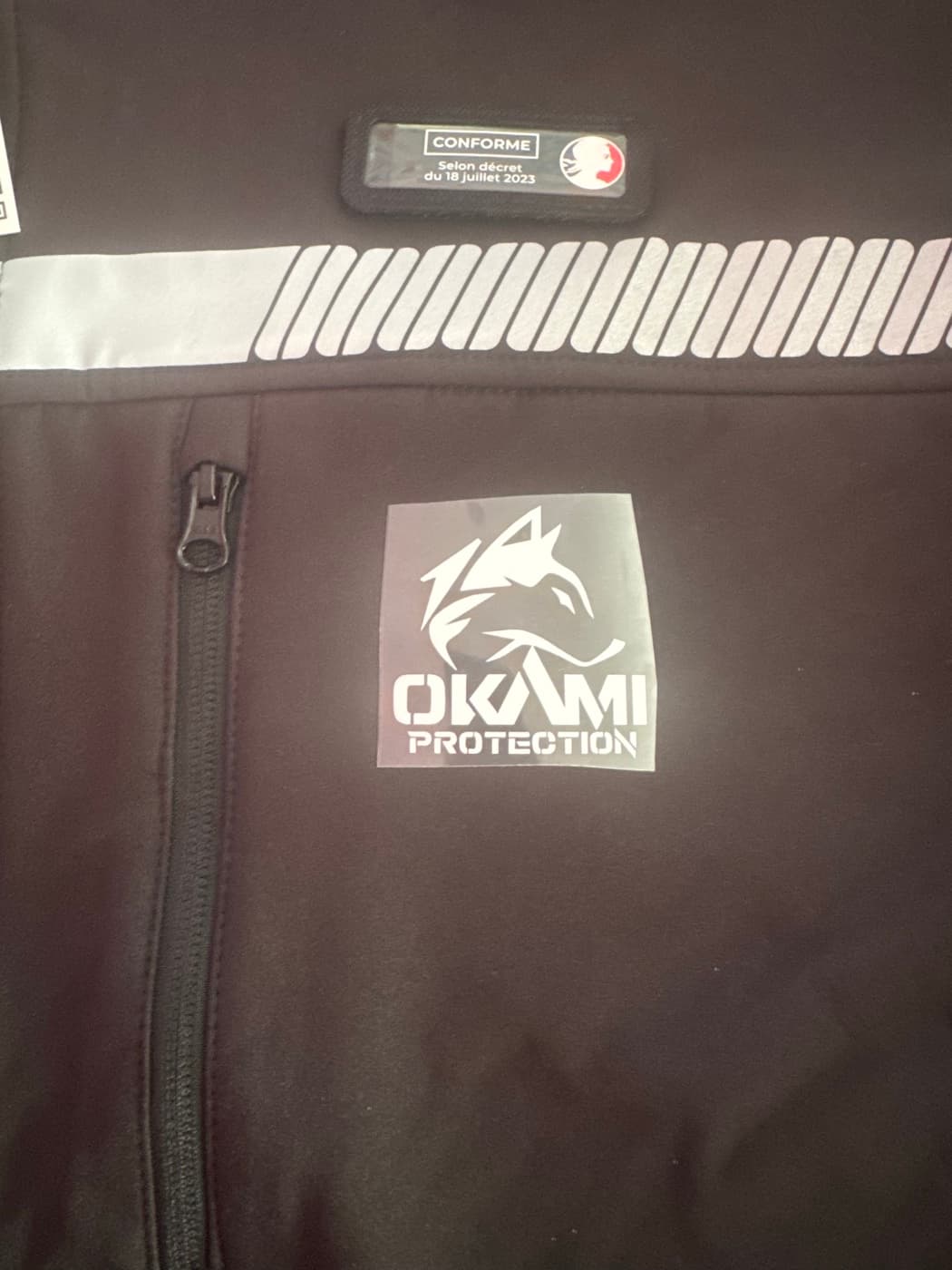 Softshell noire avec marquage Okami Protection en flex blanc et bande réfléchissante